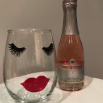 Wine glass with painted eyelashes and lips next to a small wine bottle