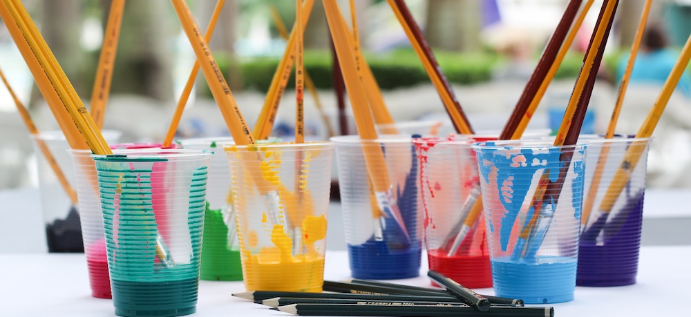 Cups of paint in different colors with paintbrushes in them